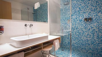Un baño moderno con un lavamanos grande de color blanco, una cabina de ducha de vidrio y una pared de azulejos con un diseño de mosaico azul.