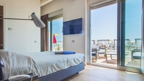 A modern hotel room with a large bed, a bedside telephone, a flat-screen TV mounted on the wall, and a sliding glass door leading to an outdoor area with seating. - Terme Beach Resort (Ravenna)