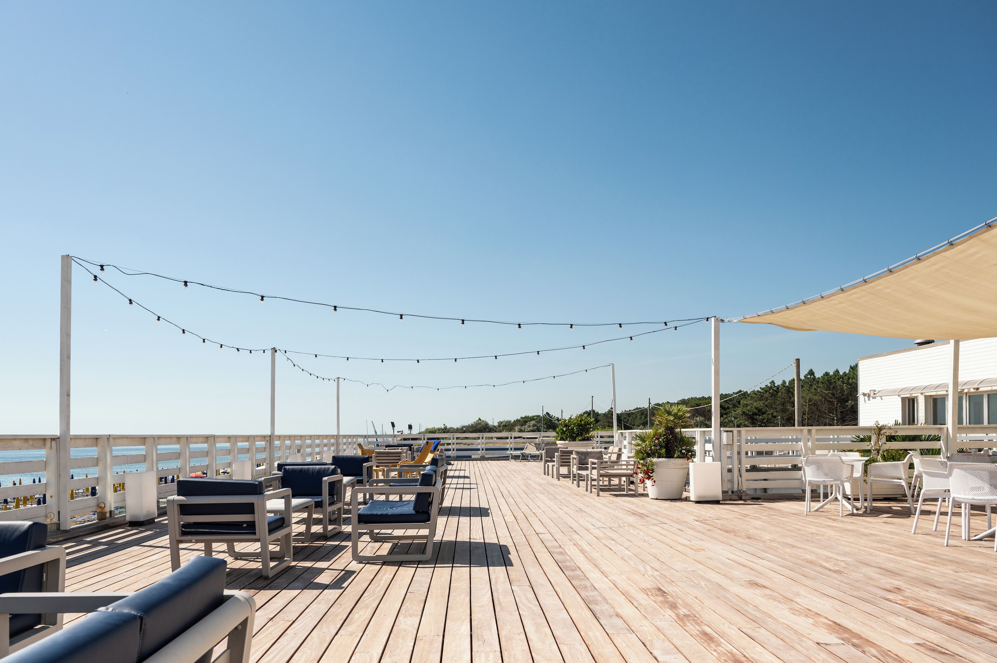 Una terraza de madera con mobiliario exterior, luces colgantes y vista al mar.