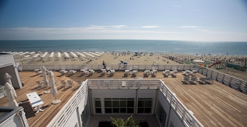 A deck with sun loungers and umbrellas overlooking a beach with people and umbrellas.