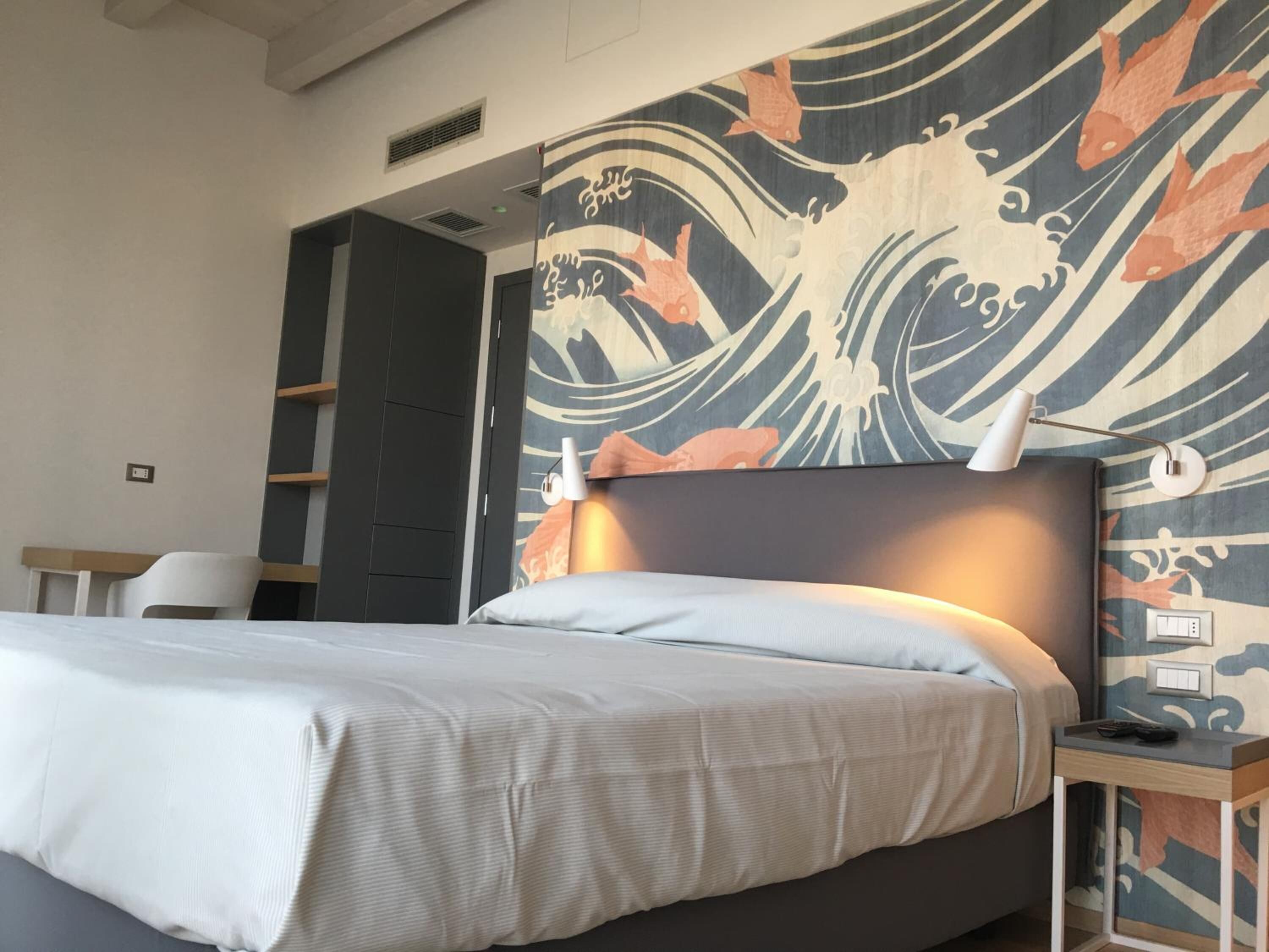 A hotel room with a bed, a nightstand, a lamp, and a wall with a wave pattern design.