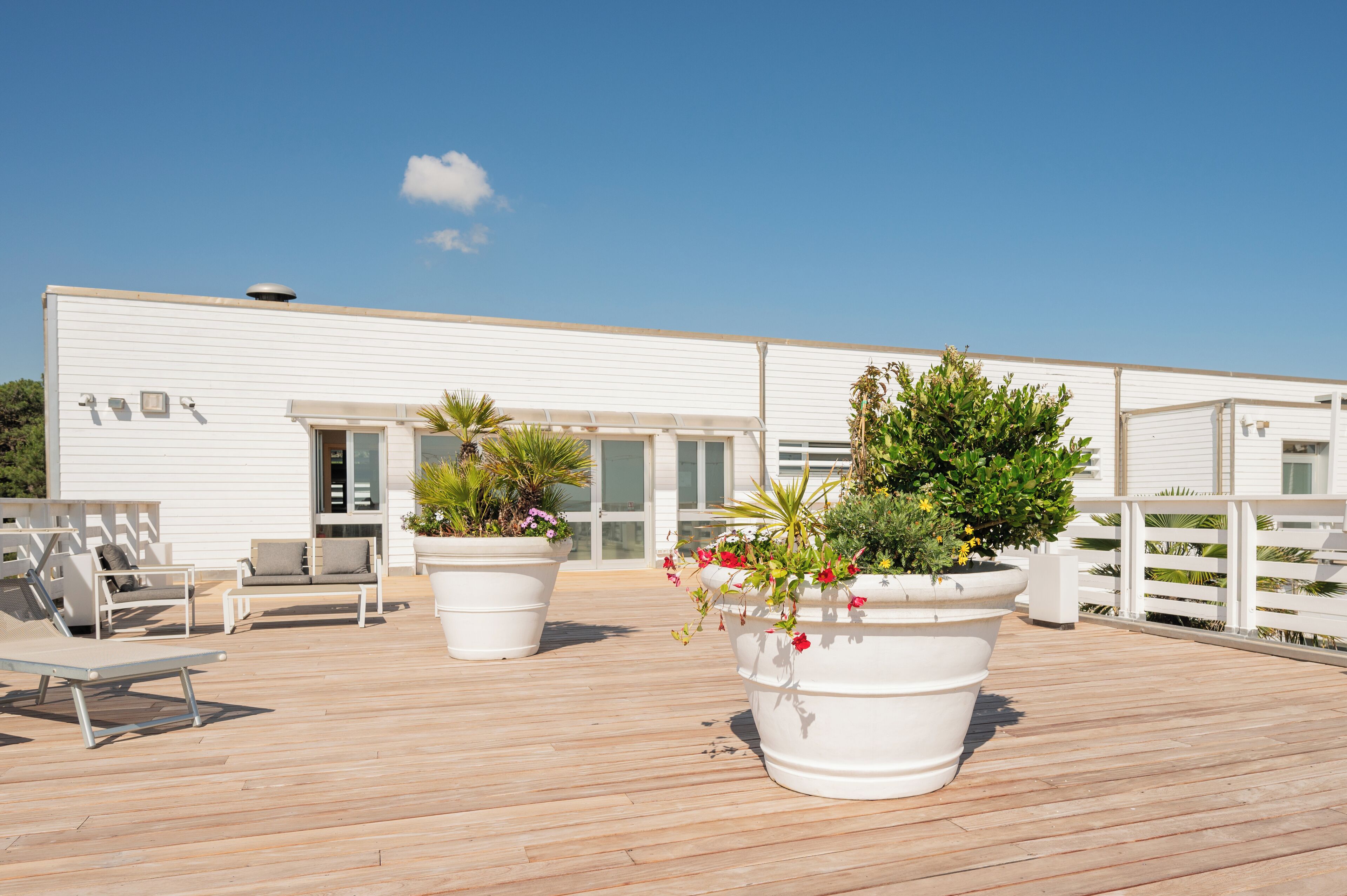 A deck with outdoor seating, potted plants, and a white building with large windows.