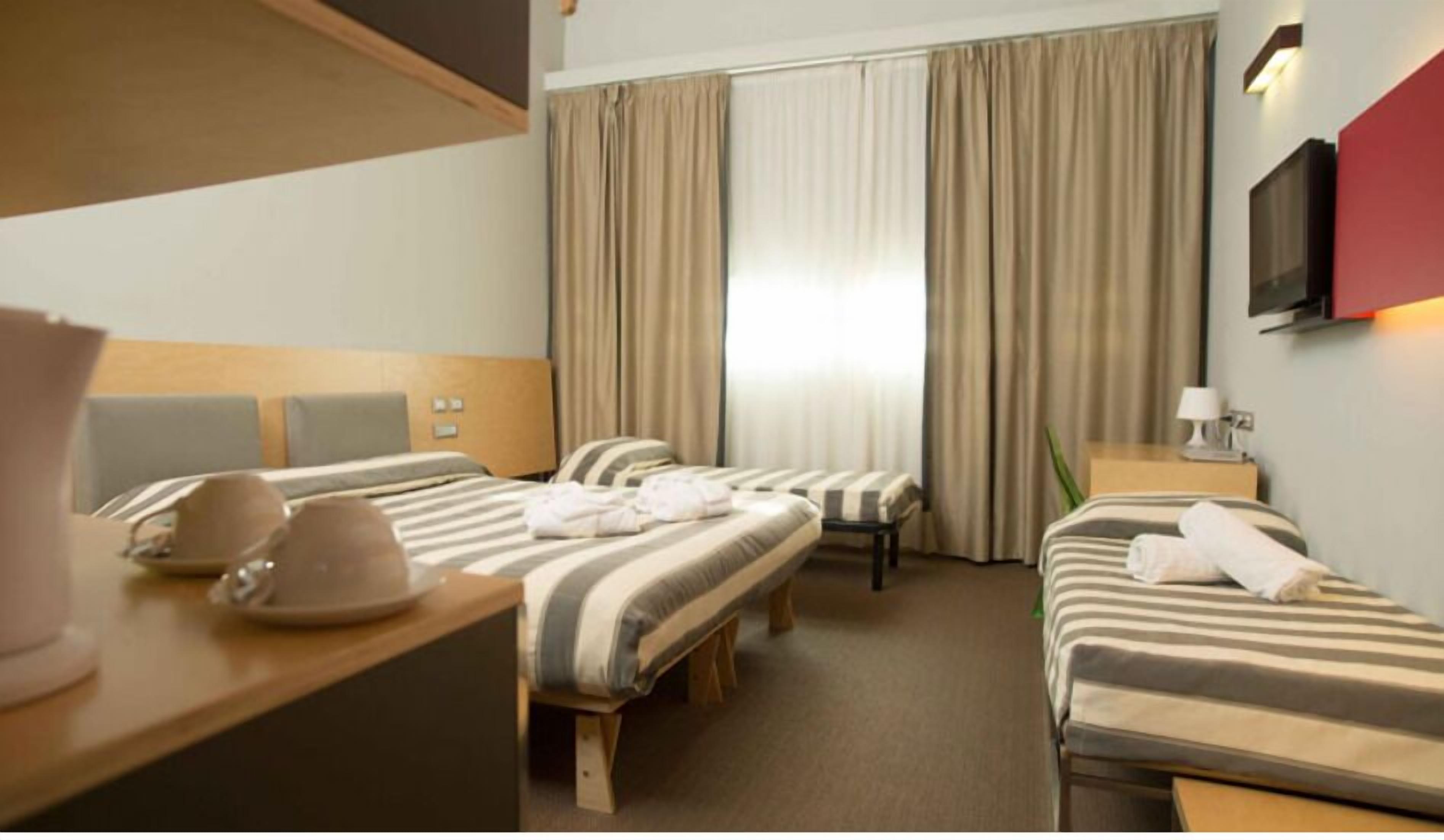 A hotel room with two beds, a desk, a chair, a TV, and a window with curtains.