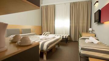 A hotel room with two beds, a desk, a chair, a TV, and a window with curtains.