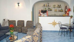 A bar area with shelves of bottles and snacks, a star decoration on the wall, and a seating area with patterned sofas and a table with chairs. - Il Gabbiano (Positano)