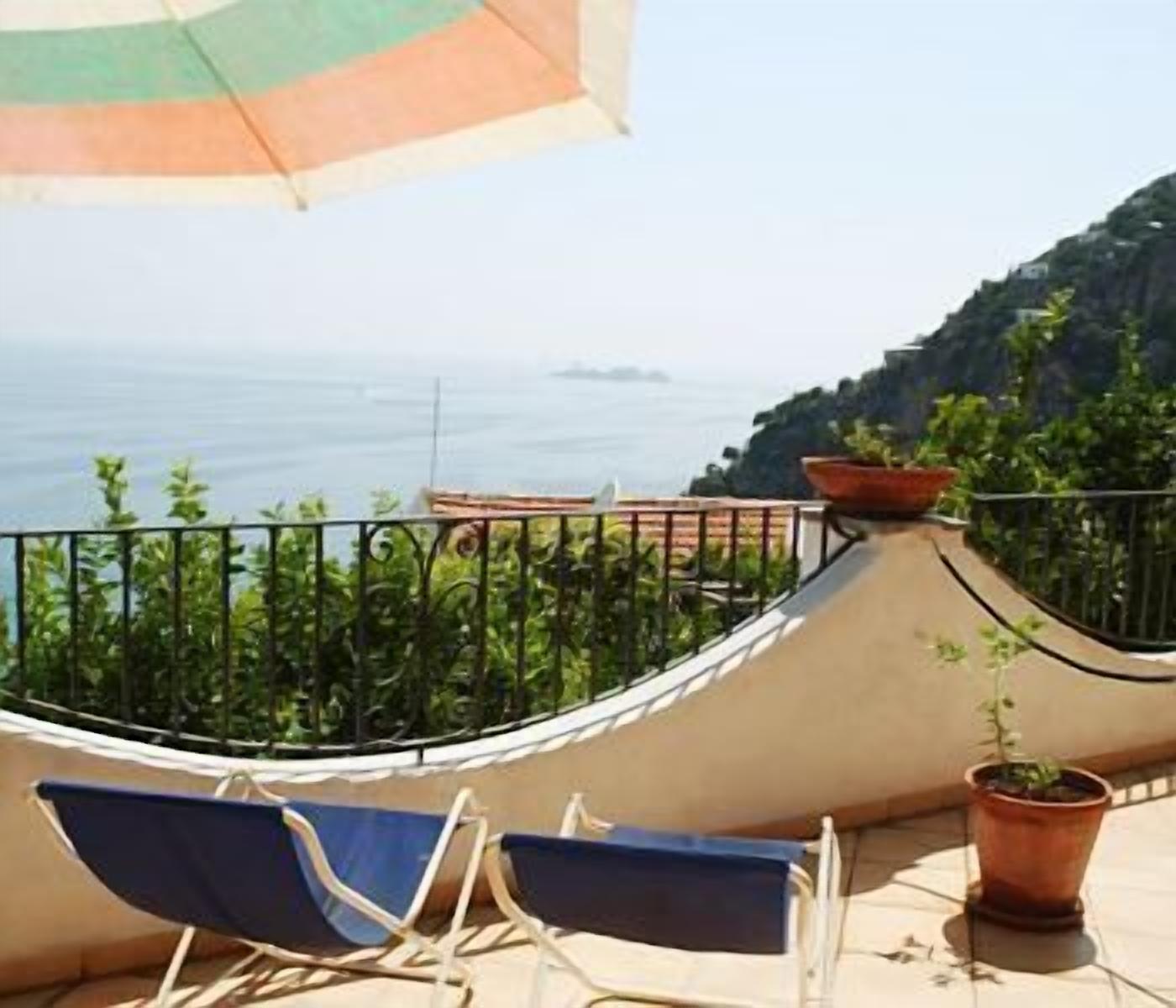 A balcony with a view of the sea, a hammock, and two lounge chairs.
