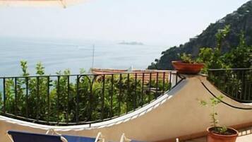 A balcony with a view of the sea, a hammock, and two lounge chairs.