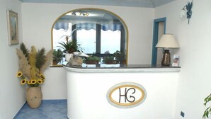 A reception area with a curved counter, a mirror above it, and a potted plant with sunflowers. - Il Gabbiano (Positano)