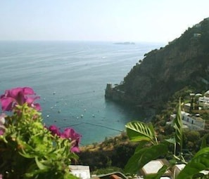 A coastal view with a rocky cliff, a clear sky, and a few boats on the water. - Il Gabbiano (Positano)