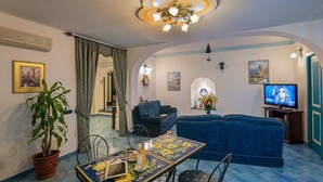 A living room with a sofa, a TV, a dining table with chairs, and a potted plant. - Il Gabbiano (Positano)