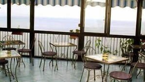 A covered outdoor seating area with tables and chairs, overlooking a body of water. - Il Gabbiano (Positano)