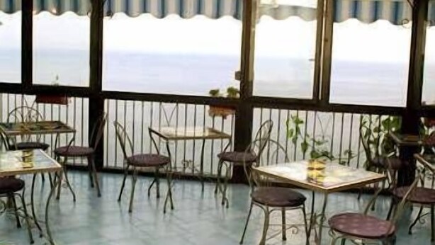 A covered outdoor seating area with tables and chairs, overlooking a body of water. - Il Gabbiano (Positano)