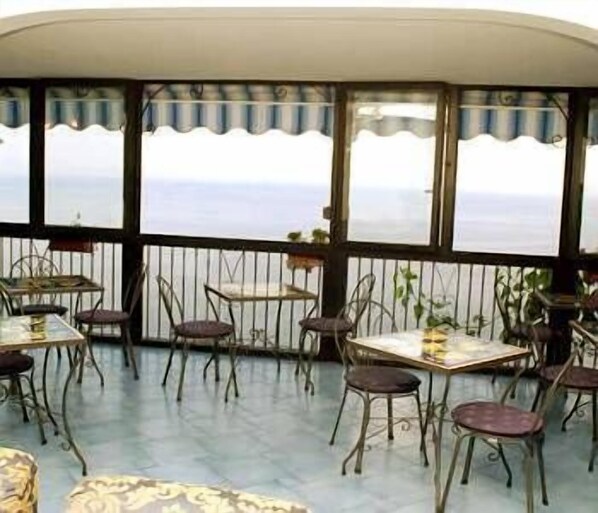 A covered outdoor seating area with tables and chairs, overlooking a body of water. - Il Gabbiano (Positano)