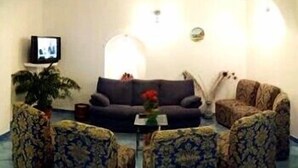 A living room with a sofa, two armchairs, a television, and a potted plant. - Il Gabbiano (Positano)
