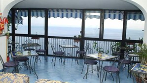 A terrace with tables and chairs, a railing, and a view of the sea. - Il Gabbiano (Positano)