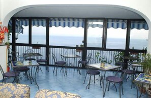 A terrace with tables and chairs, a railing, and a view of the sea. - Il Gabbiano (Positano)