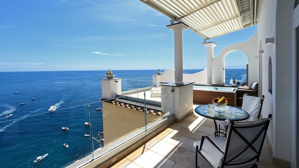 A balcony with a view of the sea, a table with chairs, and a small kitchen area.