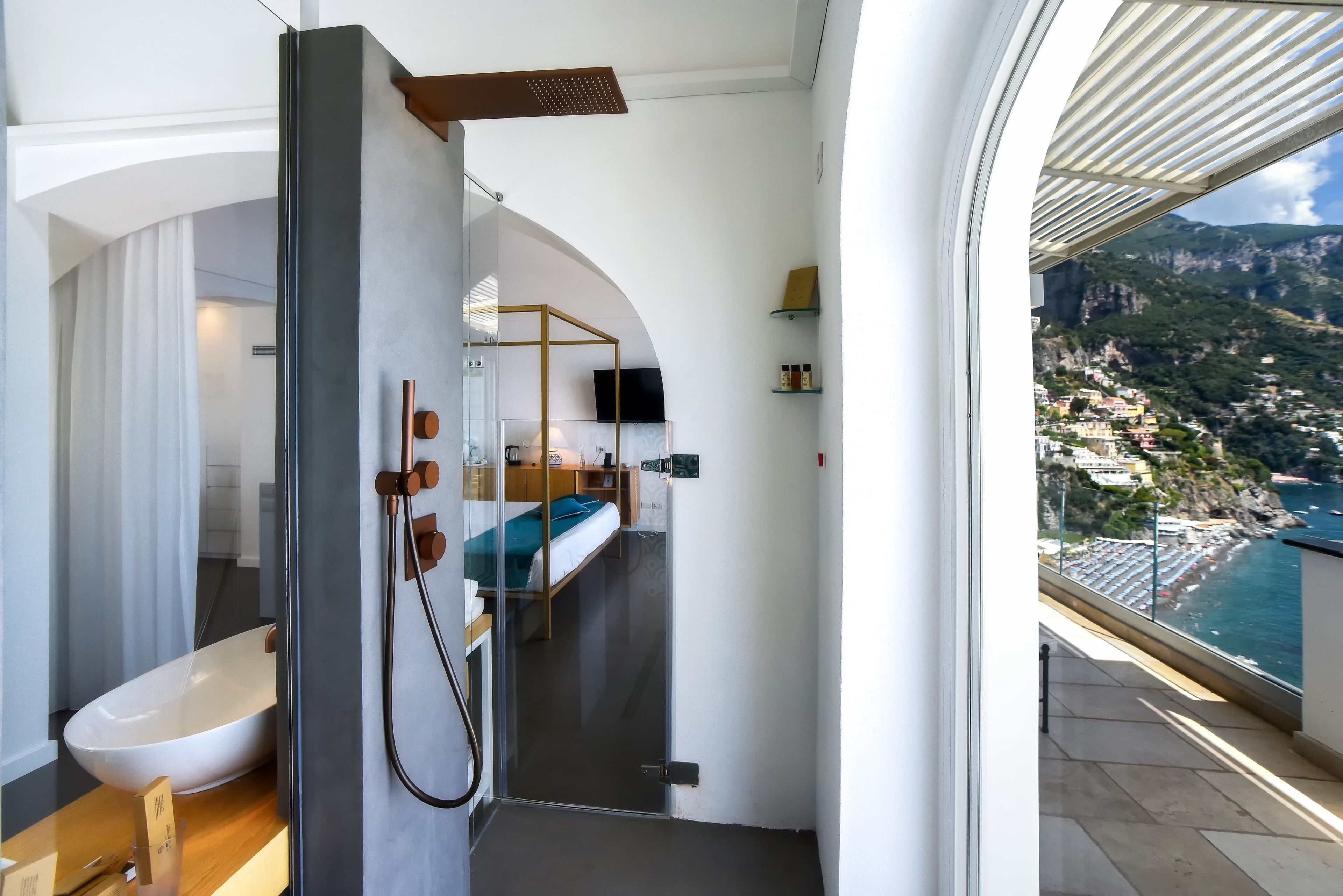 A modern bathroom with a glass shower enclosure, a white sink, and a view of a coastal town.
