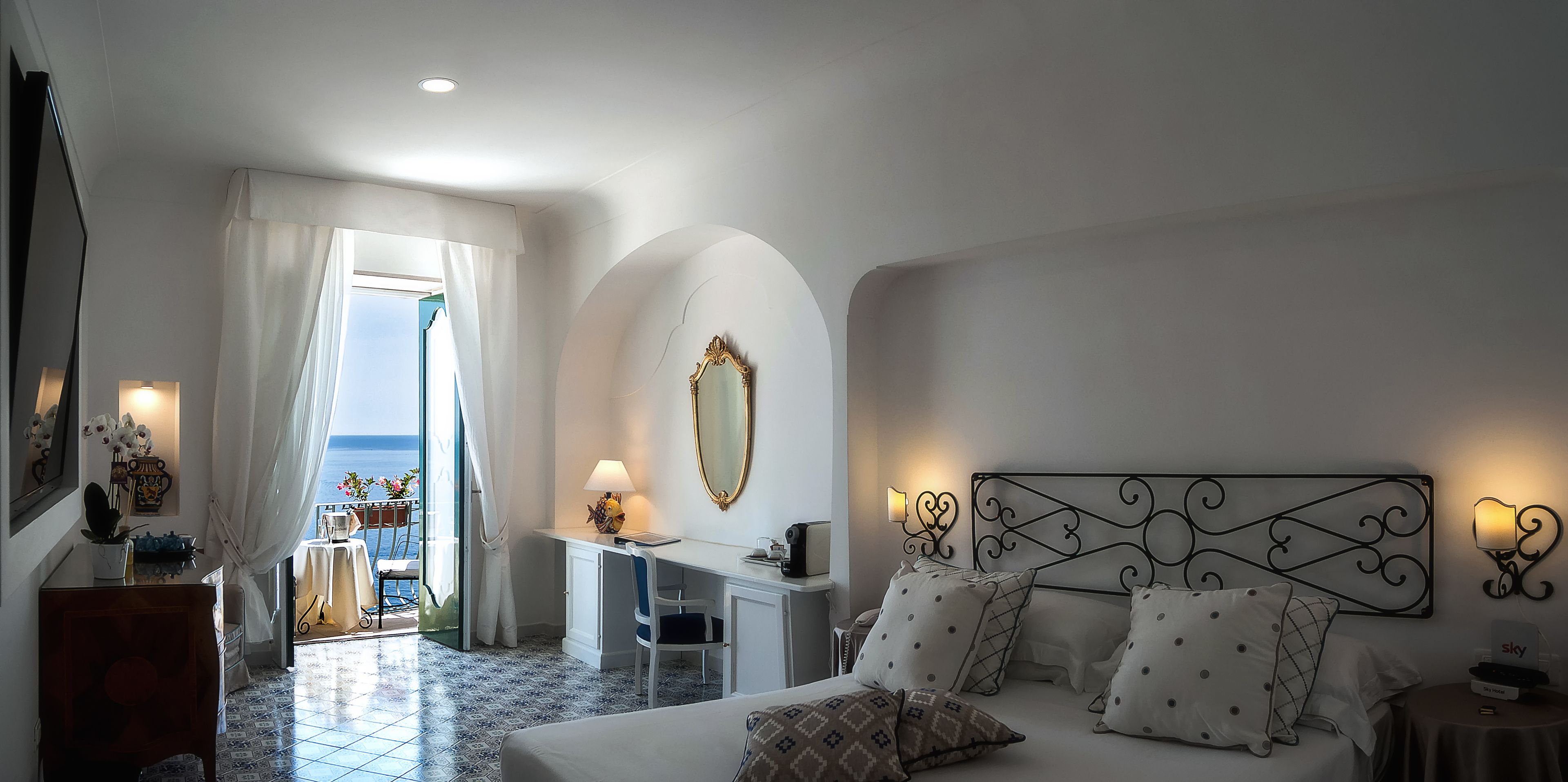 A hotel room with a bed, desk, and a view of the sea.