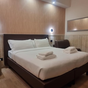 Habitación de hotel con una cama grande, cabecera de madera, luz de pared y una silla.