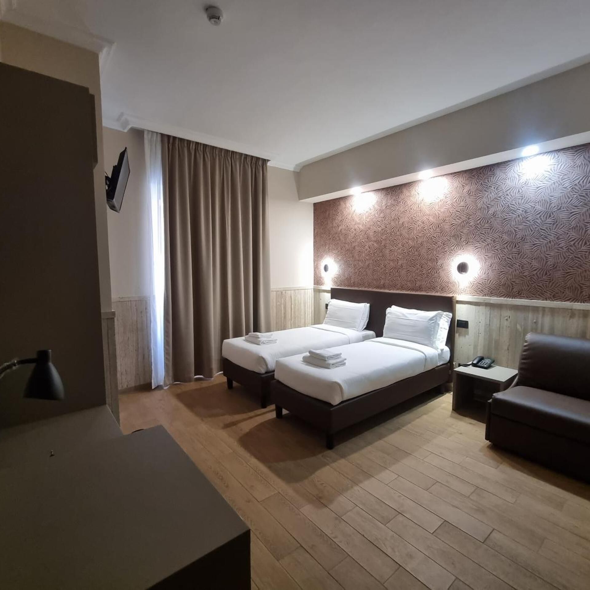 Ett hotellrum med två sängar, ett skrivbord, en stol och en vägg med ett mönster.