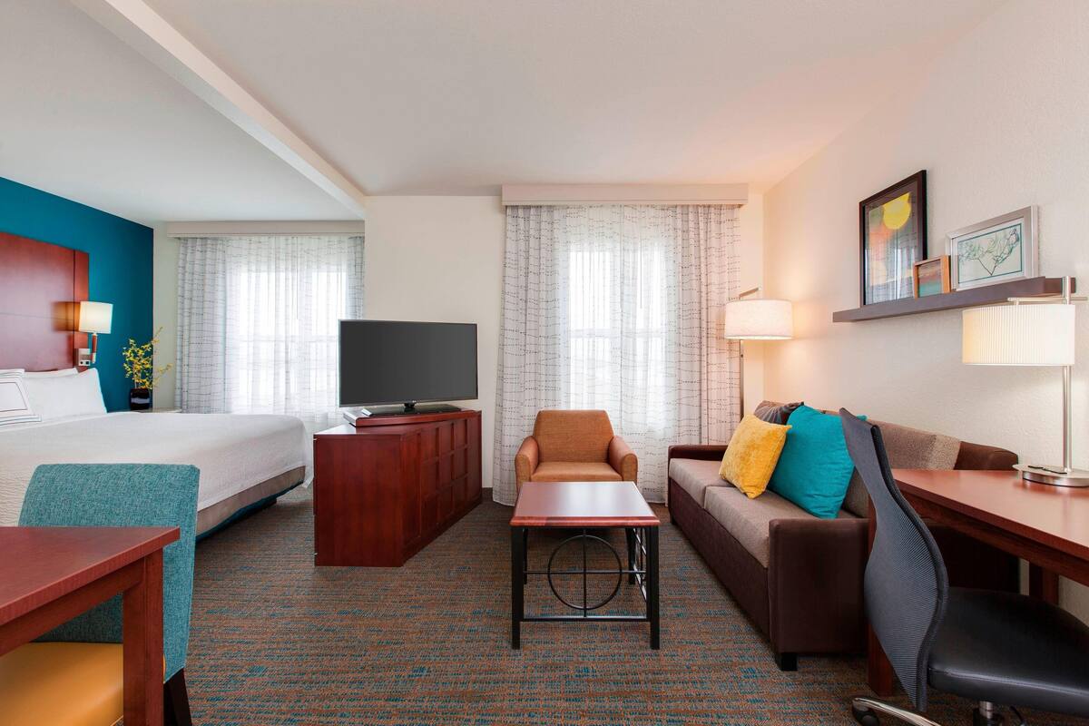A hotel room with a bed, a TV, a desk, a chair, a sofa, and a small table.