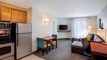 Habitación de hotel compacta con kitchenette, zona de comedor, espacio de descanso y televisor montado en la pared.