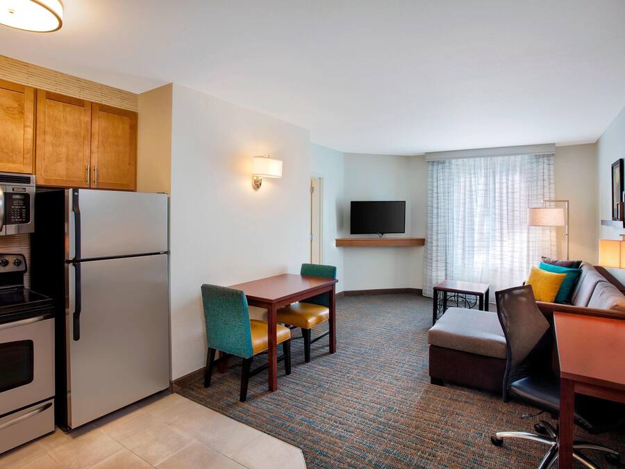 Habitación de hotel compacta con kitchenette, zona de comedor, espacio de descanso y televisor montado en la pared.
