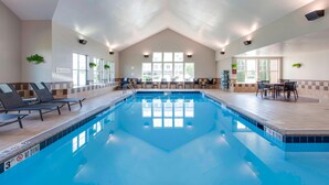 Piscina interna com placa de 'Não Mergulhar', espreguiçadeiras e área de refeições com mesas e cadeiras.