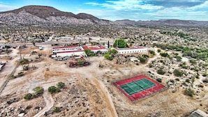 An aerial view of a desert area with buildings, a tennis court, and sparse vegetation. - Hotel Mision Catavina (Catavina)