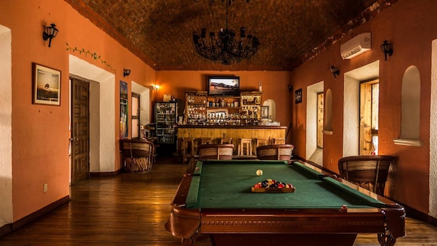 A billiards room with a pool table, chairs, and a bar area with bottles and glasses. - Hotel Mision Catavina (Catavina)