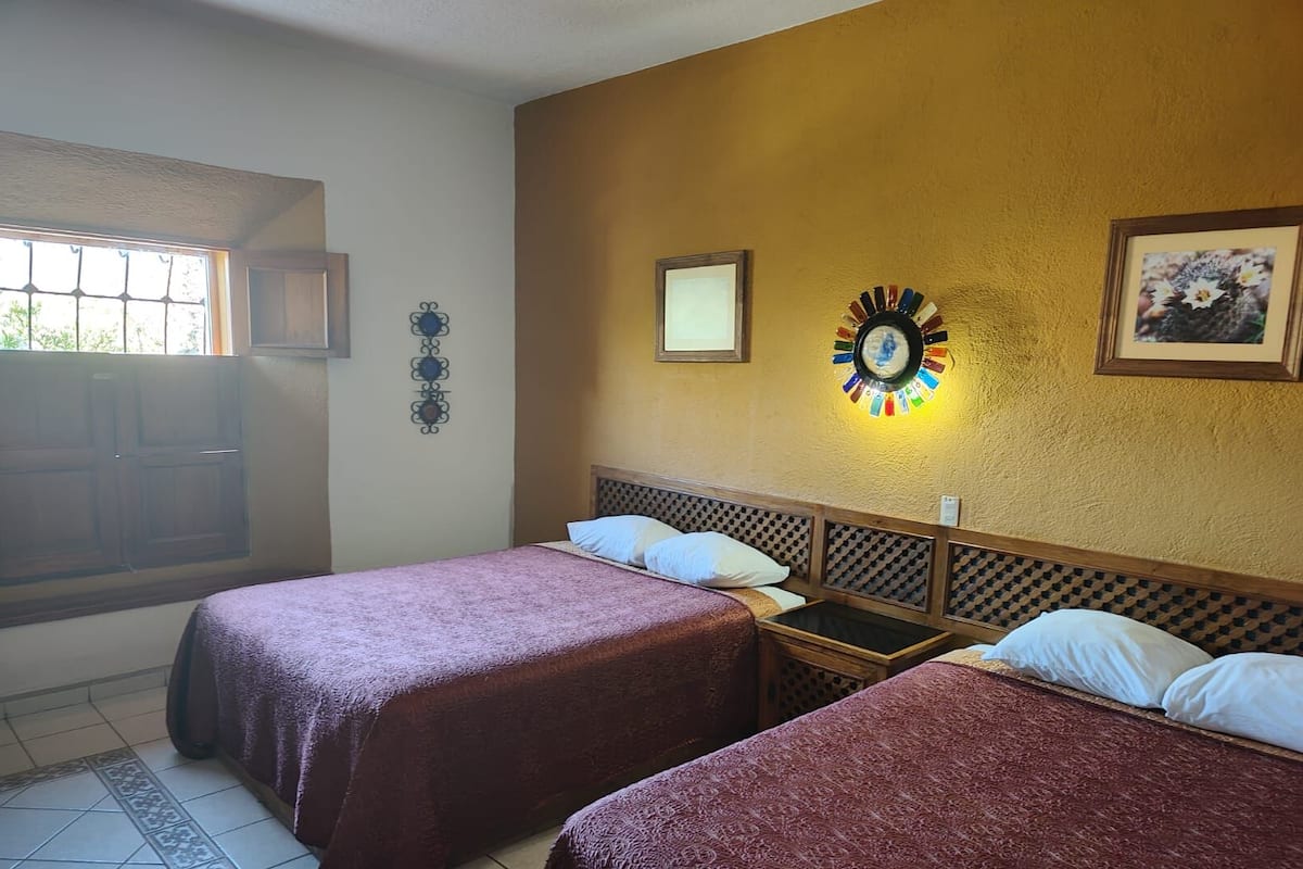 Habitació d'hotel amb dos llits, una finestra, un rellotge de paret i un quadre encimbellat.