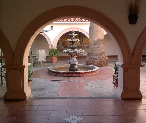 A courtyard with a central fountain, surrounded by arches and potted plants.