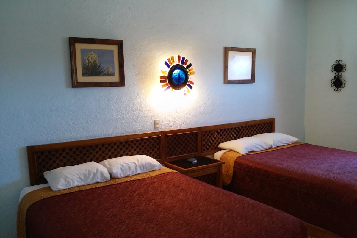 Habitació d'hotel amb dos llits, una tauleta de nit, un rellotge de paret i dos quadres amb marc.