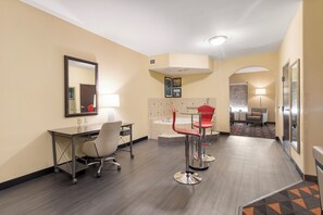 A hotel room with a desk, two red bar stools, a large mirror, a bed with a headboard, a small table with a lamp, and a hallway leading to another room. - Holiday Inn Hotel & Suites Waco Northwest by IHG (Waco)