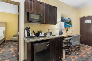 A compact kitchen with a microwave, coffee maker, and sink. There's a small refrigerator, a chair, and a desk with a lamp. - Holiday Inn Hotel & Suites Waco Northwest by IHG (Waco)