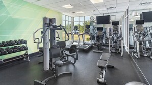 Un gimnasio con diferentes equipos de ejercicio, incluyendo cintas de correr y máquinas de pesas, además de un estante con mancuernas.