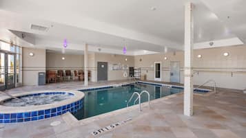 Une grande piscine intérieure dotée d’un jacuzzi, d’un revêtement de sol carrelé et d’un espace détente avec des chaises.