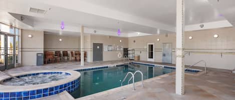 Une grande piscine intérieure dotée d’un jacuzzi, d’un revêtement de sol carrelé et d’un espace détente avec des chaises.