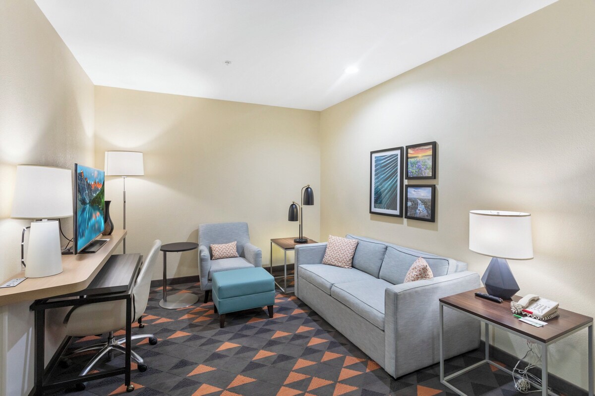A hotel room with a desk, a sofa, a chair, a small table, and a lamp.