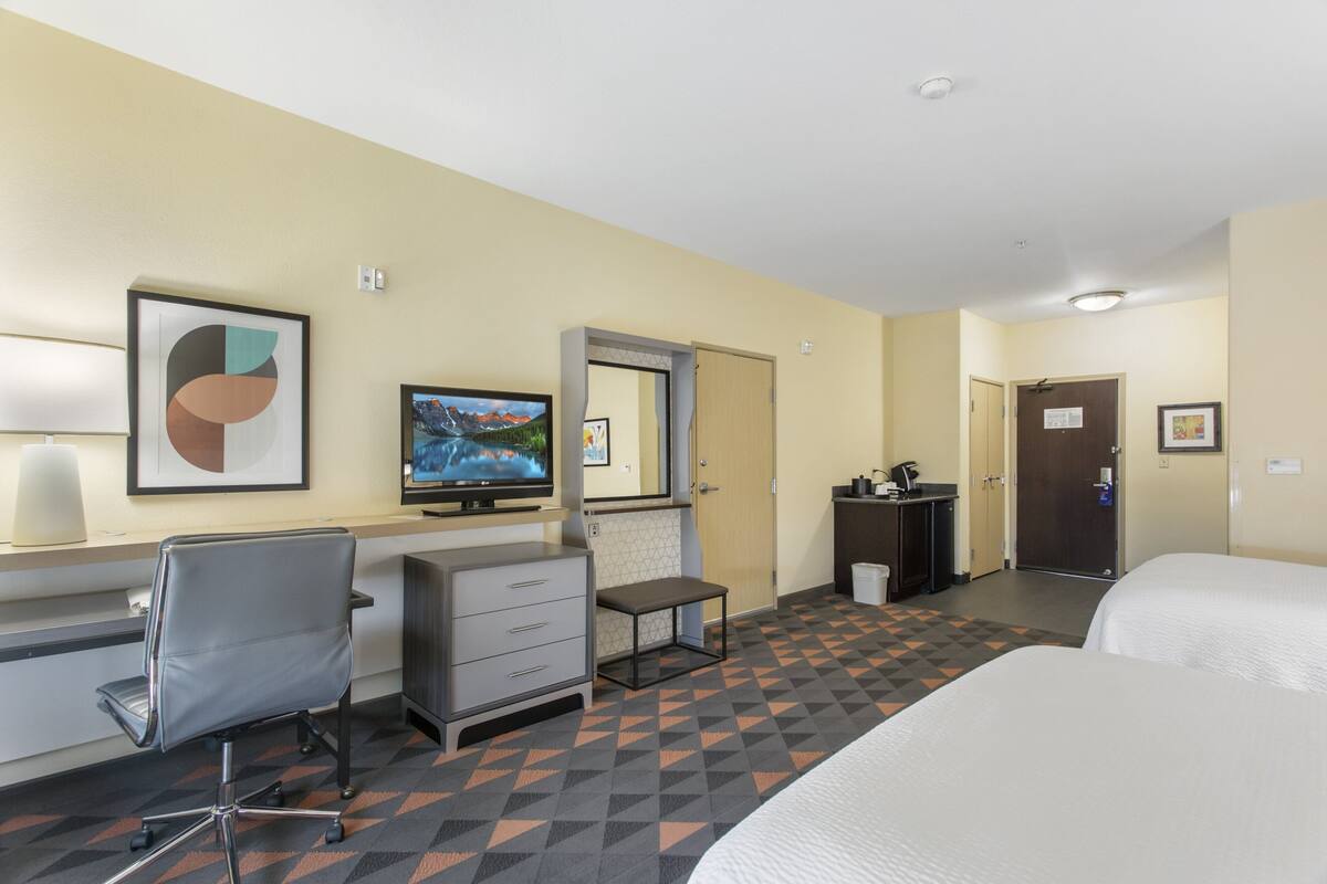 A hotel room with a bed, desk, chair, and a television.