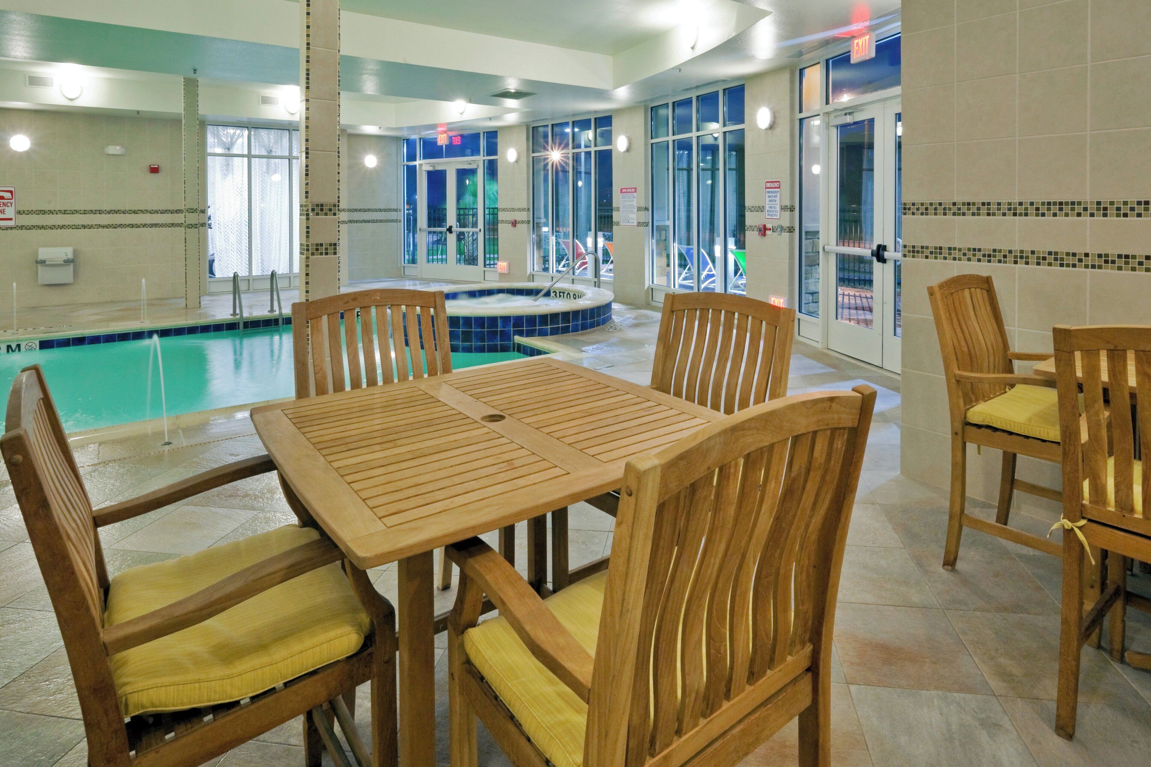 Un espace piscine comprenant un jacuzzi, des chaises en bois et une table.