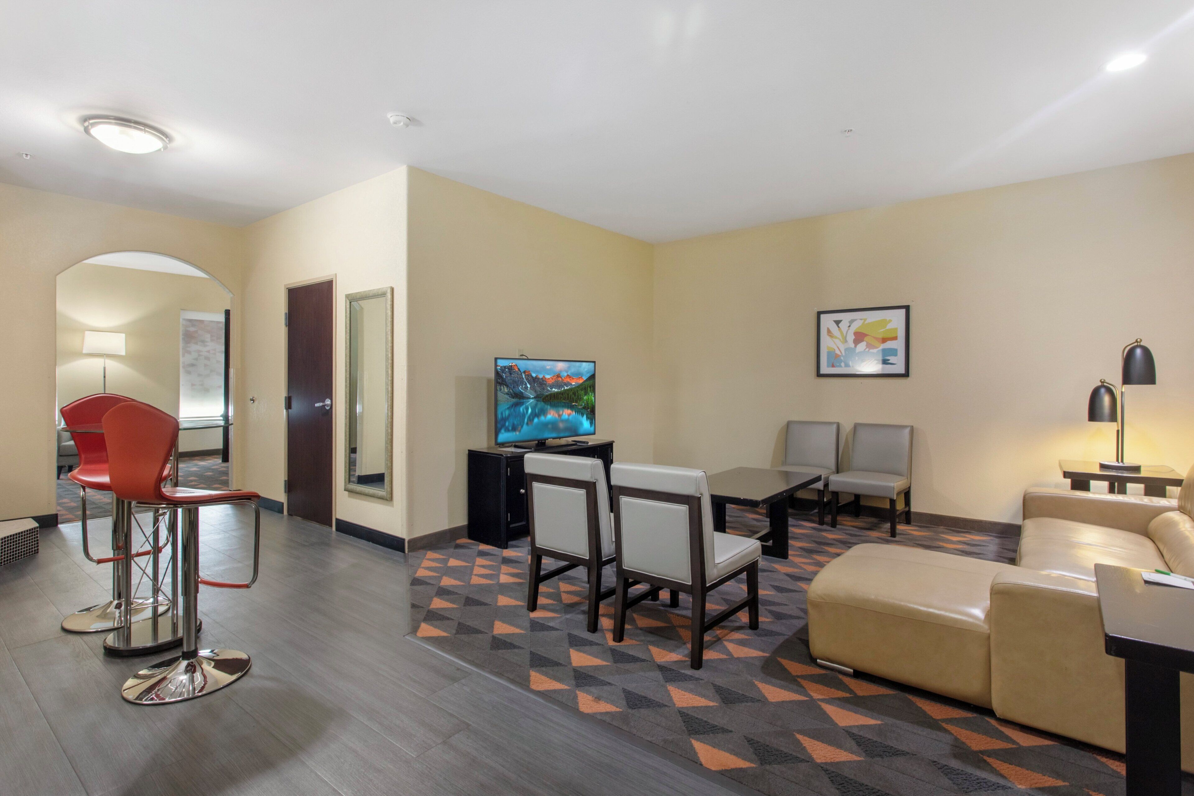 A hotel room with a TV, seating area, and a patterned carpet.