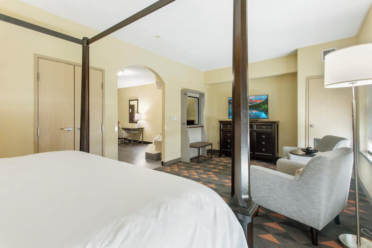 A hotel room with a large bed, a desk, a chair, a dresser, and a TV.