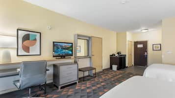 Een hotelkamer met een bed, een bureau met stoel, een televisie, een klein tafeltje en een deur.