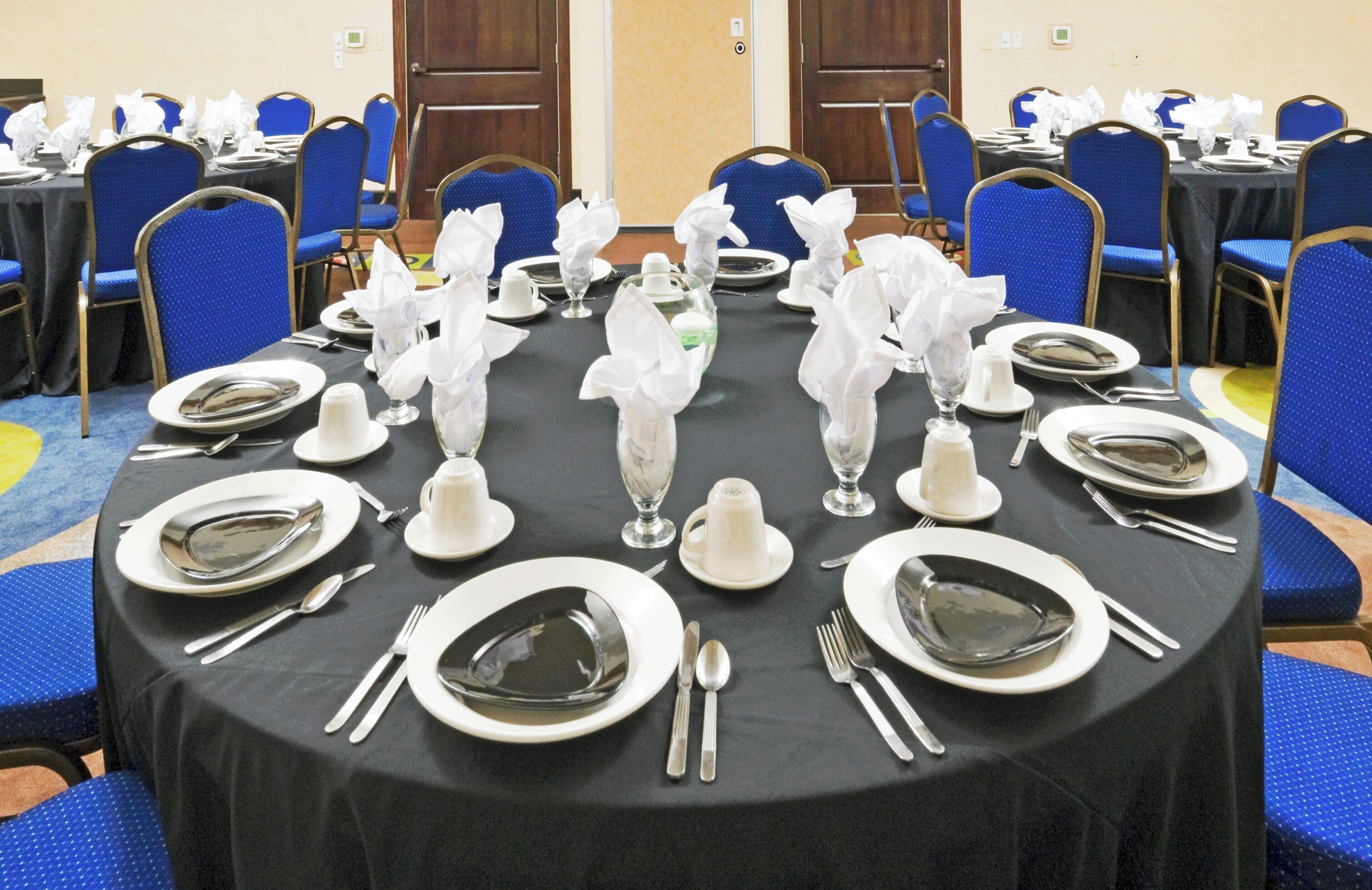 Un salón de banquetes con mesas redondas dispuestas para comer, cada una con platos, cubiertos y servilletas dobladas.
