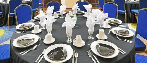 Un salón de banquetes con mesas redondas dispuestas para comer, cada una con platos, cubiertos y servilletas dobladas.
