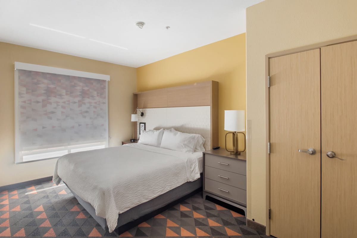 A hotel room with a bed, a nightstand, a lamp, a wardrobe, and a window with blinds.