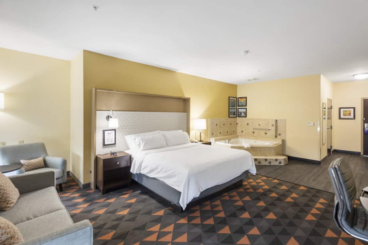 A hotel room with a bed, a sofa, a desk, a nightstand, a lamp, a bathroom with a bathtub, and a shower.