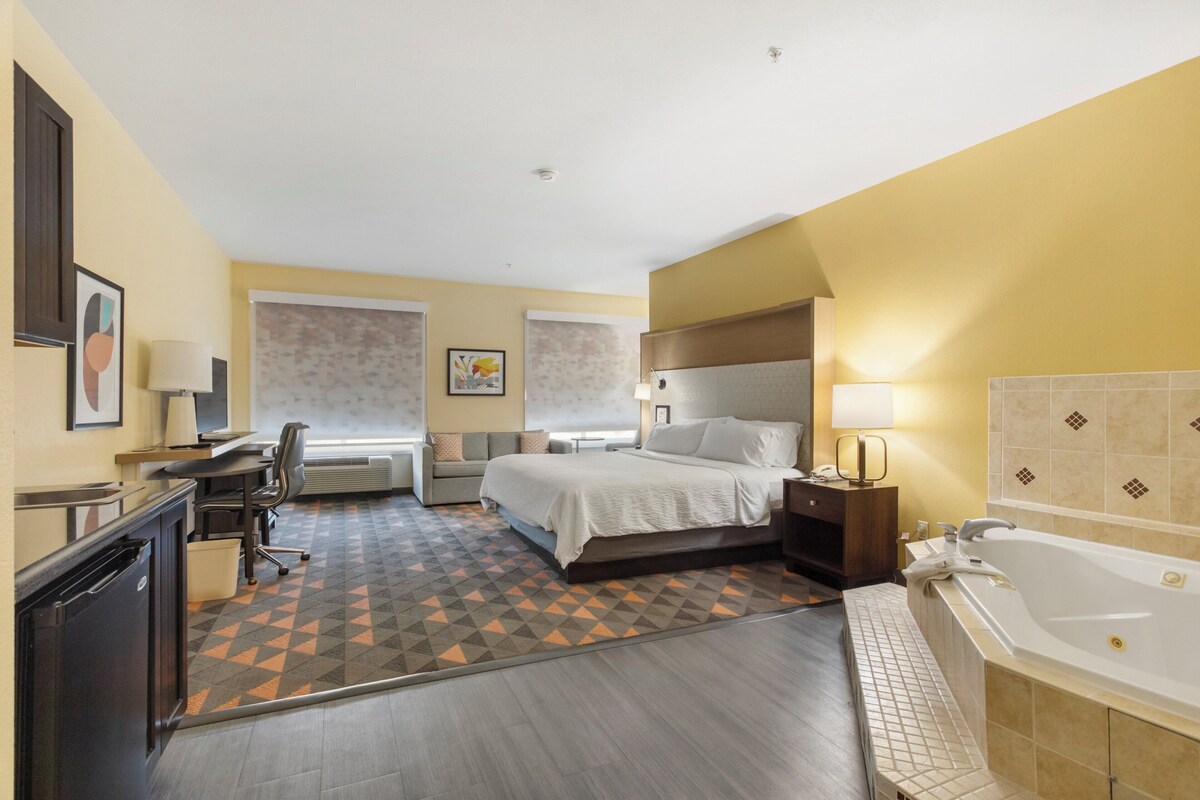 A hotel room with a bed, desk, chair, and a large bathtub.